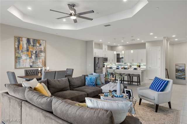 tiled living room featuring ceiling fan and a raised ceiling