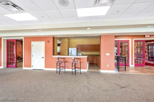 kitchen featuring a breakfast bar, a paneled ceiling, french doors, light colored carpet, and white refrigerator with ice dispenser