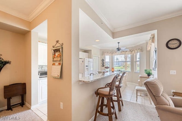 kitchen featuring white fridge with ice dispenser, crown molding, a breakfast bar, light tile patterned floors, and white cabinetry