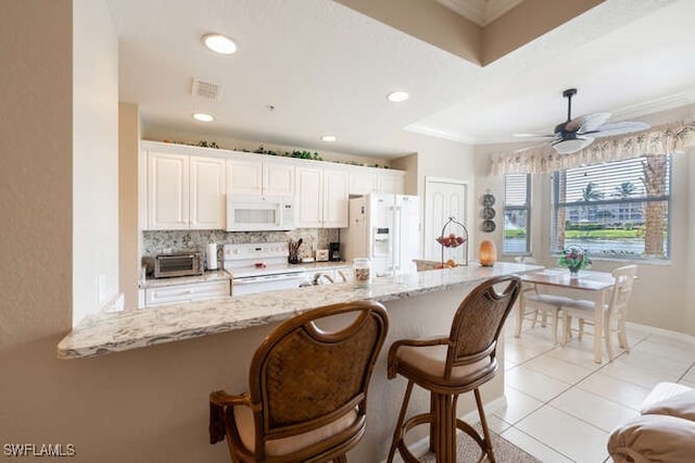 kitchen featuring white appliances, light stone counters, a breakfast bar area, and ceiling fan