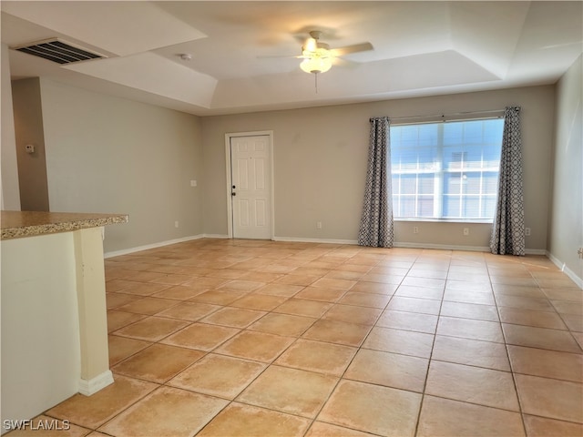 tiled empty room featuring ceiling fan and a raised ceiling