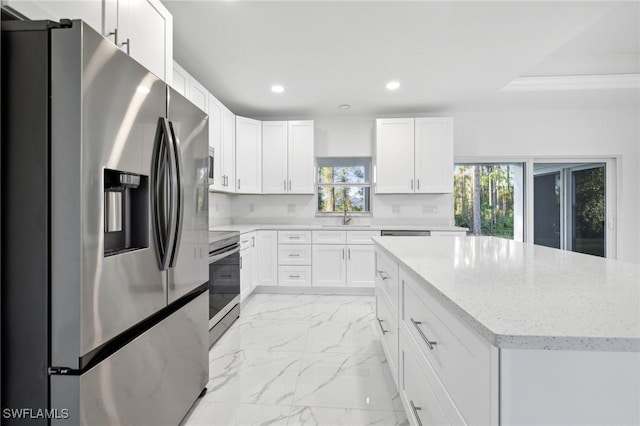 kitchen with appliances with stainless steel finishes, a healthy amount of sunlight, white cabinets, light stone counters, and sink