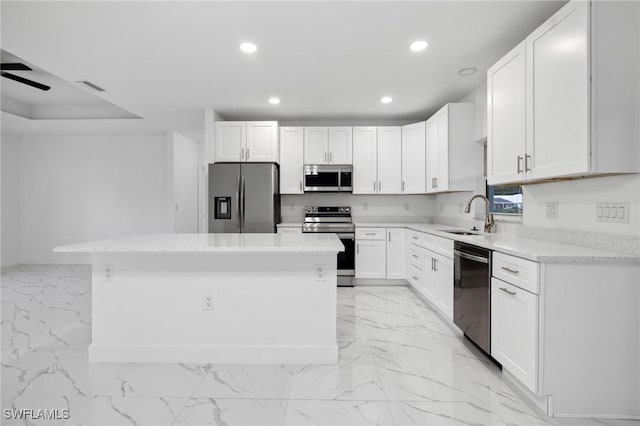 kitchen with appliances with stainless steel finishes, sink, white cabinetry, and a kitchen island