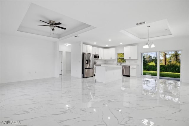 kitchen with appliances with stainless steel finishes, a raised ceiling, white cabinets, and pendant lighting