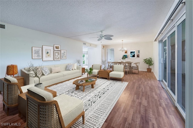 living room featuring ceiling fan with notable chandelier, dark wood-type flooring, and a textured ceiling