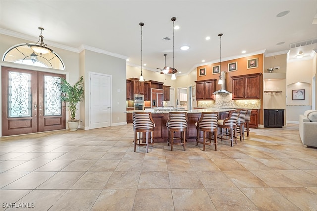 kitchen with french doors, a spacious island, wall chimney exhaust hood, decorative light fixtures, and a breakfast bar