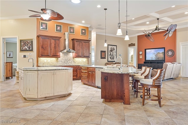 kitchen featuring wall chimney range hood, ornamental molding, beamed ceiling, and an island with sink