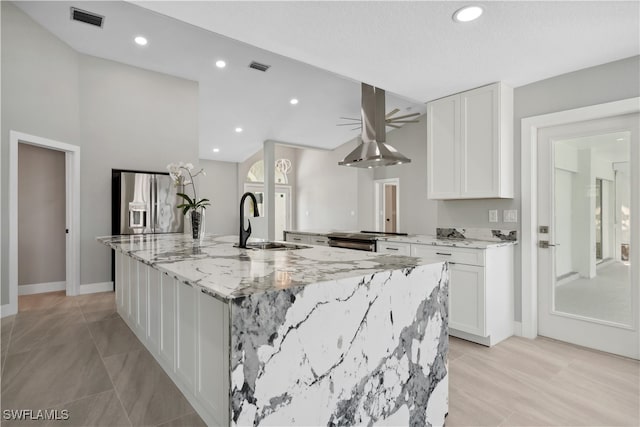 kitchen with white cabinets, light stone countertops, stainless steel appliances, and a large island with sink