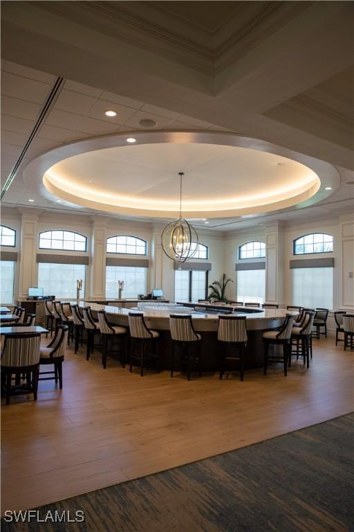 dining area with a raised ceiling, wood-type flooring, a healthy amount of sunlight, and a chandelier