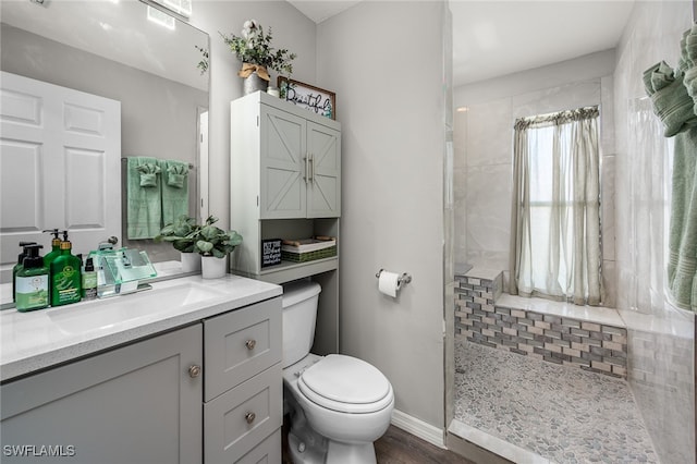 bathroom featuring vanity, hardwood / wood-style floors, toilet, and tiled shower