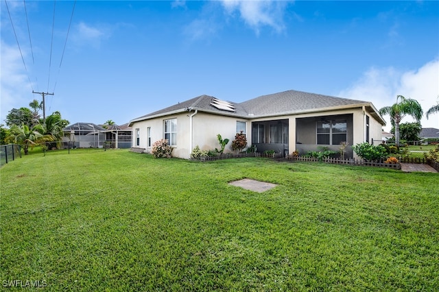 back of property with glass enclosure, a sunroom, and a lawn