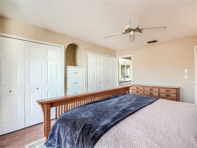 bedroom with wood-type flooring, two closets, and ceiling fan