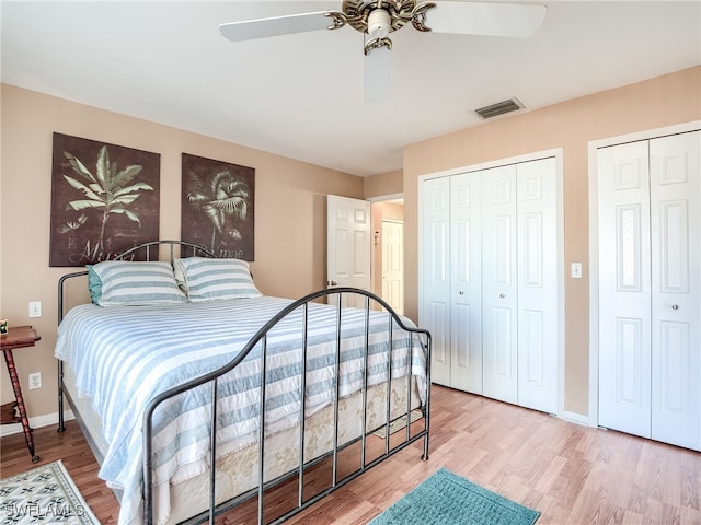 bedroom featuring two closets, hardwood / wood-style flooring, and ceiling fan