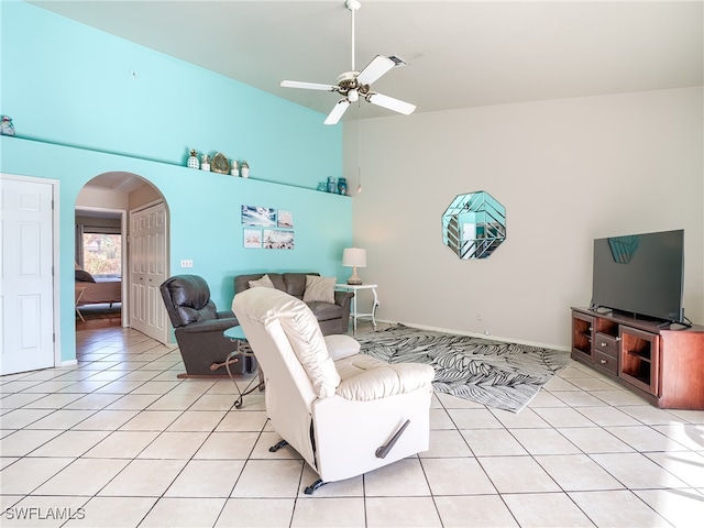 living room featuring light tile patterned floors, ceiling fan, and a towering ceiling