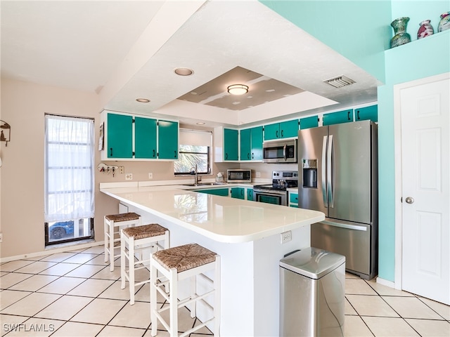 kitchen featuring stainless steel appliances, a breakfast bar, light tile patterned floors, a tray ceiling, and a kitchen island