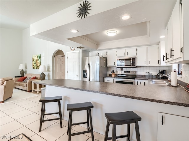 kitchen featuring a kitchen bar, white cabinets, sink, a tray ceiling, and appliances with stainless steel finishes