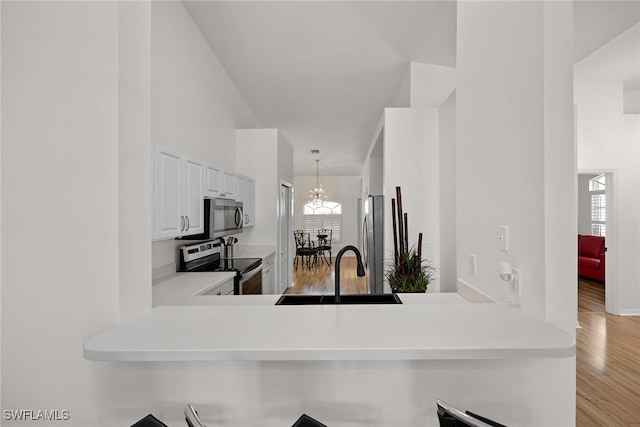 kitchen with white cabinetry, sink, stainless steel appliances, light hardwood / wood-style flooring, and kitchen peninsula