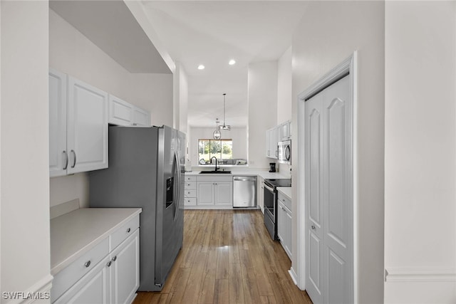 kitchen featuring stainless steel appliances, sink, light hardwood / wood-style floors, white cabinetry, and hanging light fixtures