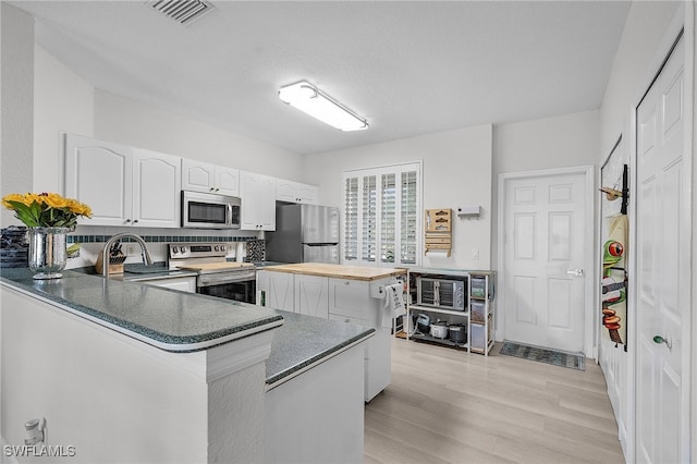 kitchen with kitchen peninsula, stainless steel appliances, light wood-type flooring, white cabinetry, and a textured ceiling