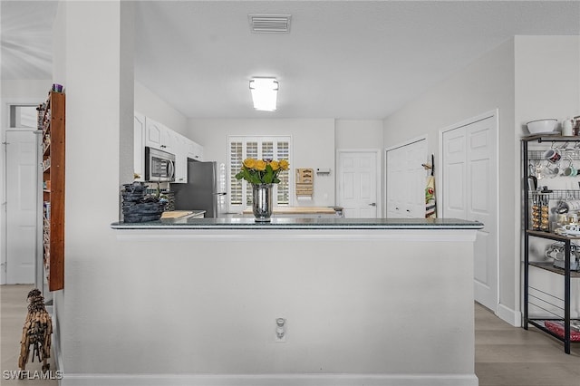 kitchen with light hardwood / wood-style flooring, kitchen peninsula, white cabinets, and stainless steel appliances