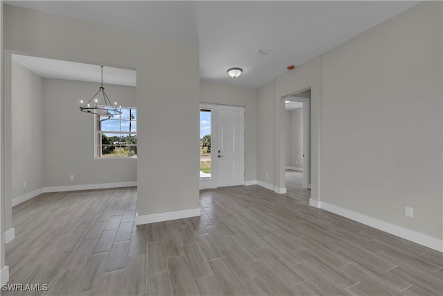 unfurnished room with a notable chandelier and light hardwood / wood-style flooring