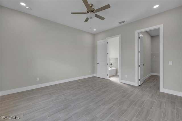 unfurnished bedroom with a closet, ensuite bath, a spacious closet, light wood-type flooring, and ceiling fan