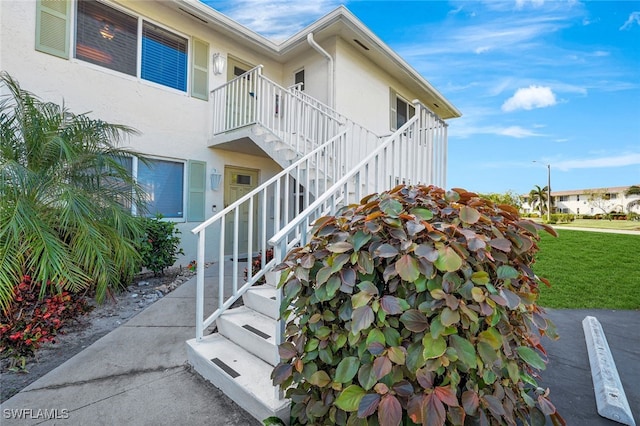 view of side of home with stairway, a yard, and stucco siding