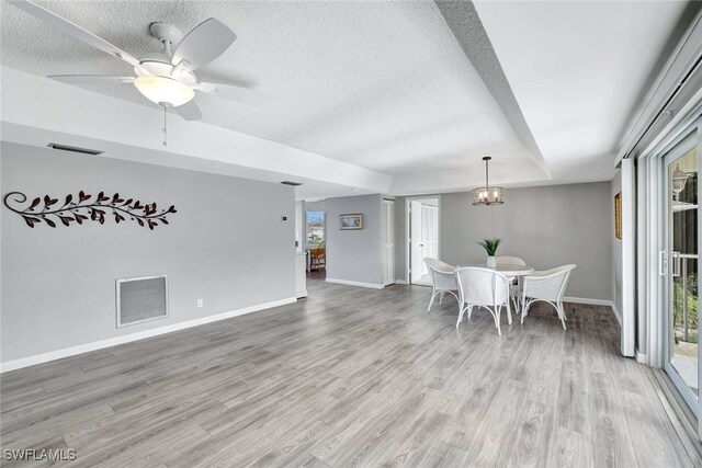 dining area with ceiling fan with notable chandelier, a raised ceiling, a textured ceiling, and light hardwood / wood-style floors