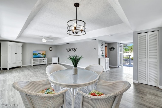 dining room with ceiling fan with notable chandelier, a tray ceiling, and wood-type flooring