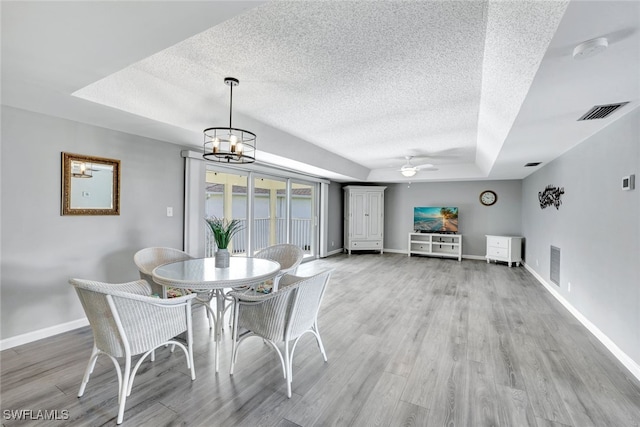 unfurnished dining area featuring ceiling fan with notable chandelier, a textured ceiling, a tray ceiling, and wood-type flooring