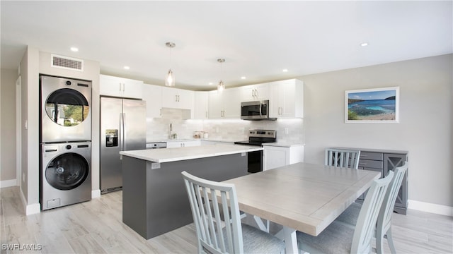 kitchen with stacked washing maching and dryer, a kitchen island, appliances with stainless steel finishes, hanging light fixtures, and white cabinets