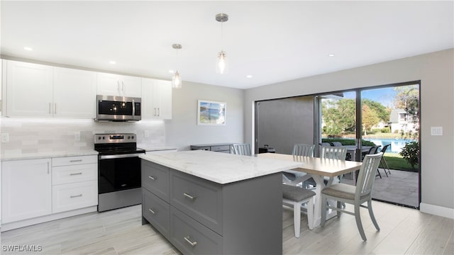 kitchen featuring stainless steel appliances, white cabinetry, pendant lighting, light stone countertops, and a center island