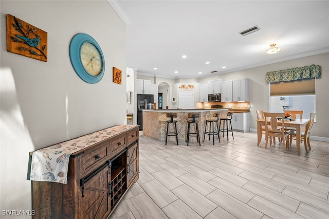 kitchen featuring a breakfast bar, a center island, white cabinetry, and black refrigerator with ice dispenser