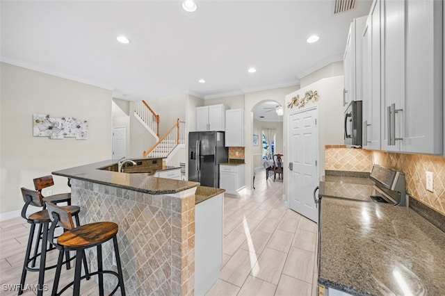 kitchen featuring a breakfast bar, stainless steel appliances, sink, dark stone countertops, and white cabinetry