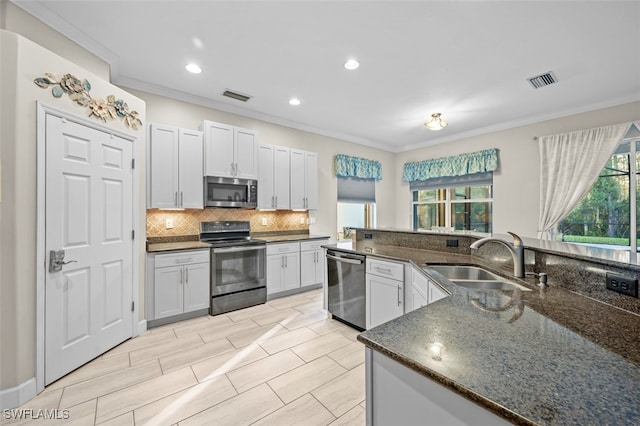 kitchen featuring white cabinetry, sink, stainless steel appliances, crown molding, and dark stone counters