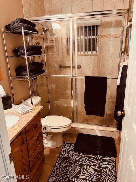 bathroom with tile patterned floors, a shower with door, vanity, and toilet