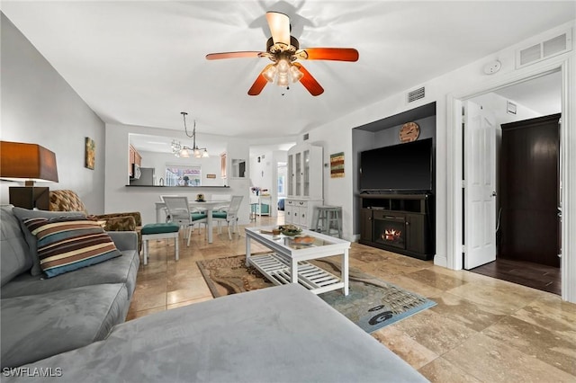 tiled living room with ceiling fan with notable chandelier