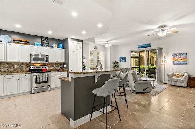 kitchen featuring stainless steel appliances, a wealth of natural light, white cabinets, and a center island with sink