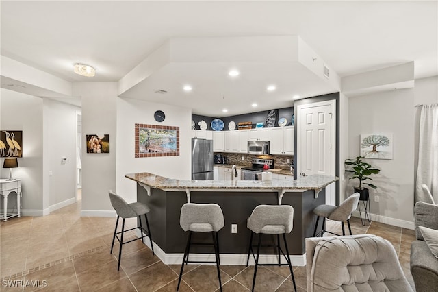 kitchen with white cabinets, a kitchen bar, stainless steel appliances, and light stone counters