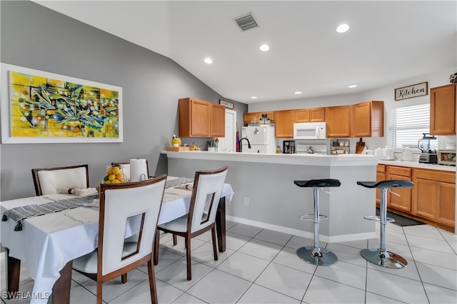 kitchen with a kitchen breakfast bar, light tile patterned floors, vaulted ceiling, and white appliances