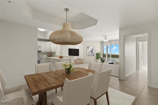 dining area featuring a raised ceiling, light tile patterned floors, and ceiling fan