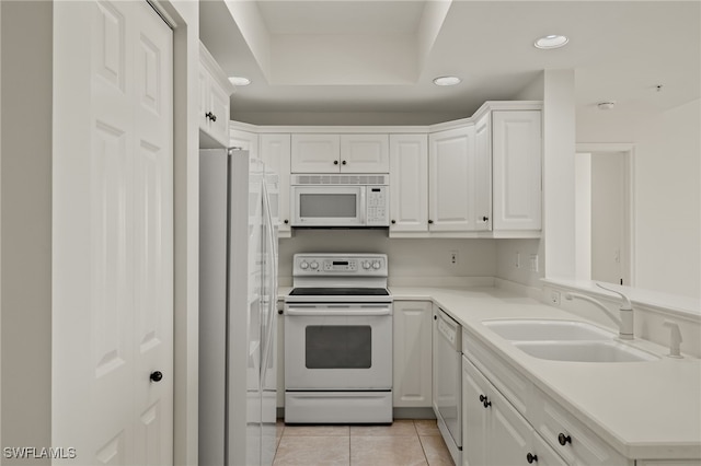 kitchen featuring sink, white appliances, light tile patterned floors, white cabinets, and a raised ceiling