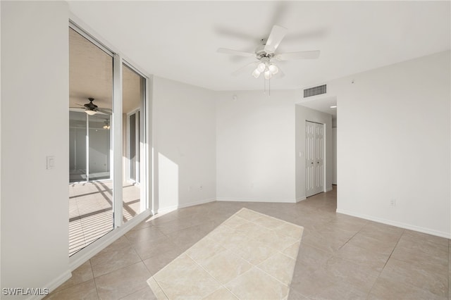 tiled empty room featuring expansive windows and ceiling fan