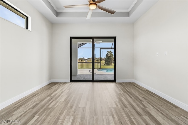 empty room with crown molding, ceiling fan, light wood-type flooring, and a raised ceiling