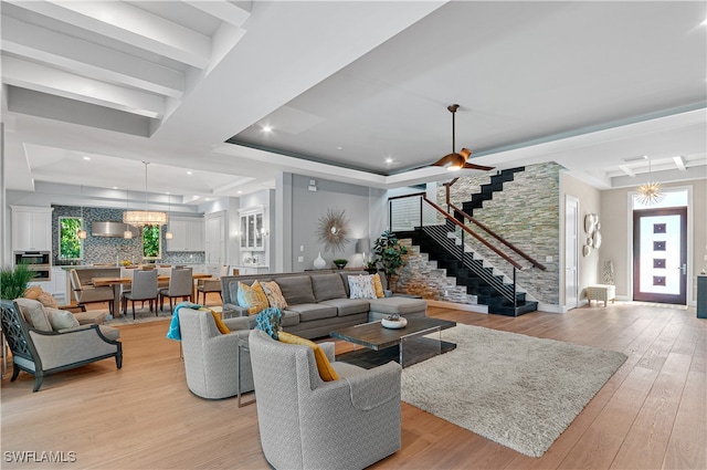 living room featuring light wood-type flooring, ceiling fan, and a raised ceiling