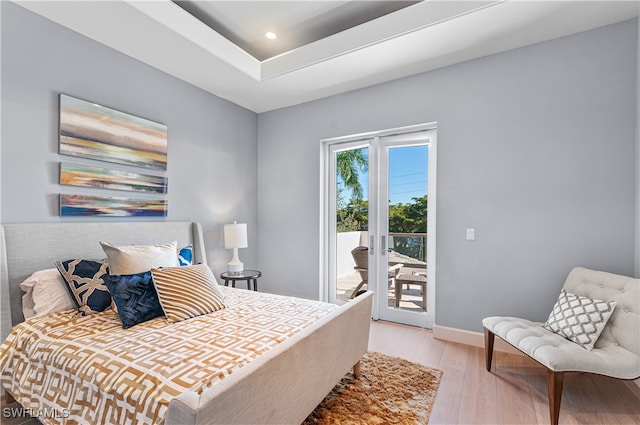 bedroom with access to exterior, a tray ceiling, light hardwood / wood-style flooring, and french doors