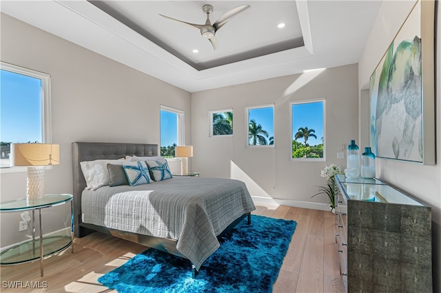 bedroom featuring ceiling fan, a tray ceiling, and light hardwood / wood-style flooring