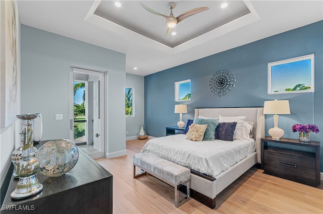 bedroom featuring ceiling fan, access to exterior, light hardwood / wood-style floors, and a raised ceiling