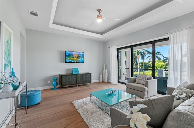 living room featuring a raised ceiling, light wood-type flooring, and ceiling fan