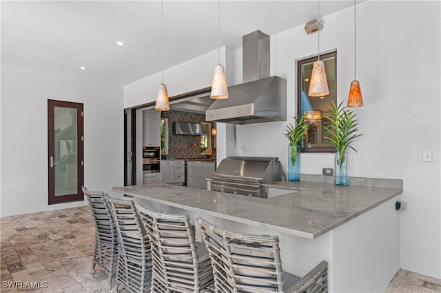 kitchen with kitchen peninsula, ventilation hood, backsplash, decorative light fixtures, and wall chimney exhaust hood